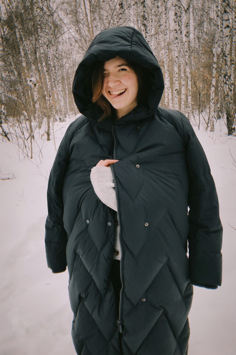 Young woman in a long puffer coat in a snowy forest