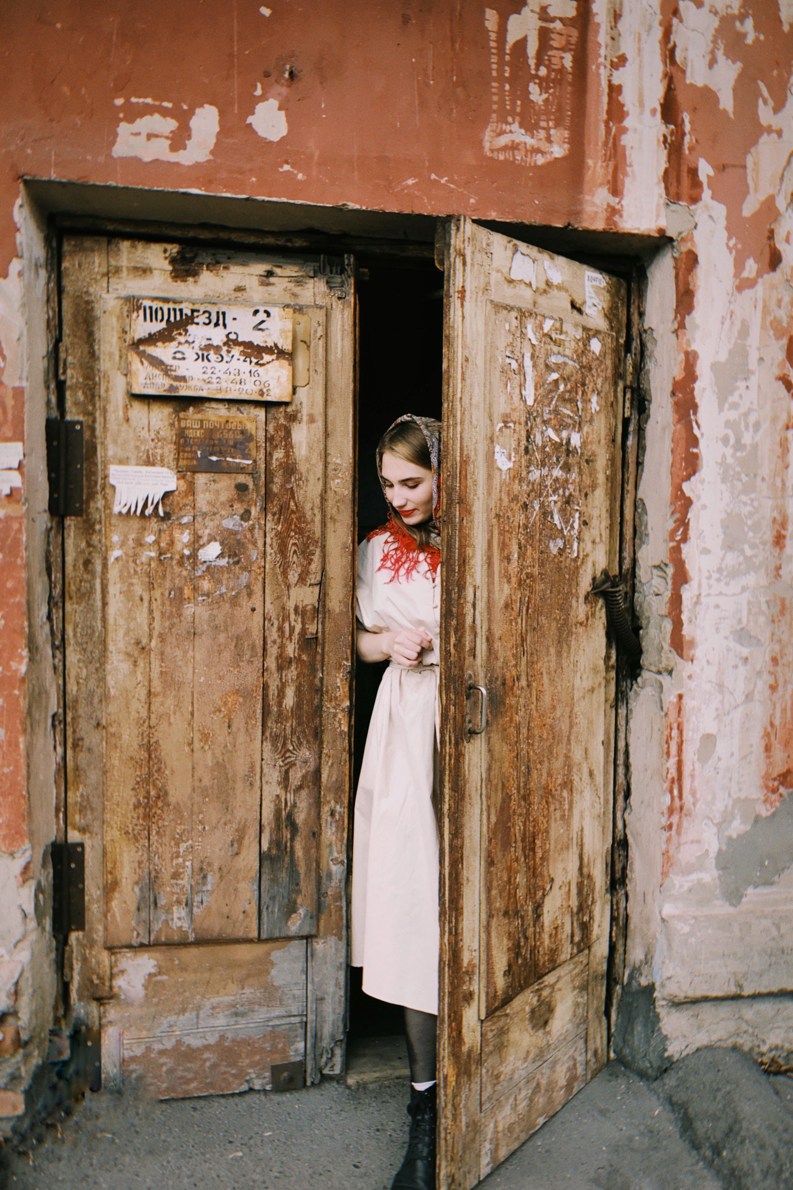 Young woman in traditional clothing stands at an old wooden doorway.