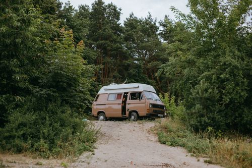 Free Explore the outdoors with a retro camper van parked on a forest path surrounded by lush greenery. Stock Photo