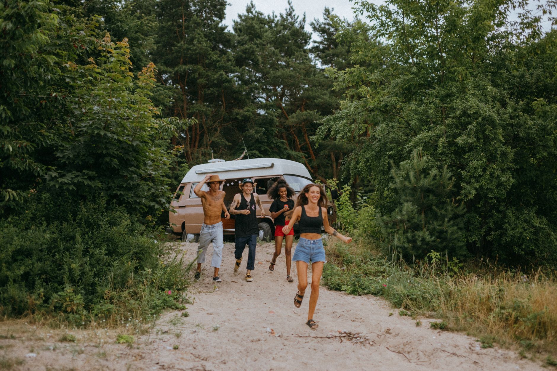Young friends enjoying a sunny day outdoors by their van, running and smiling.