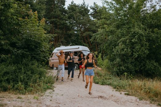 Young friends enjoying a sunny day outdoors by their van, running and smiling.