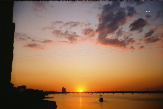 A beautiful sunset over a tranquil river with reflections and a silhouette of a boat.