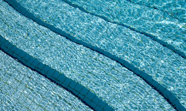 Pool Maintenance โ A detailed view of crystal clear swimming pool water over a tiled surface, showcasing its calm and refreshing nature.