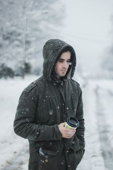 A man in a black jacket holds a coffee cup during a snowy winter day outdoors.