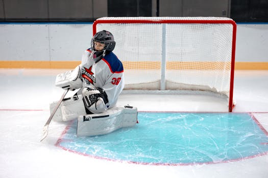 Ice hockey goalie in full gear kneeling on the ice to defend the goal.