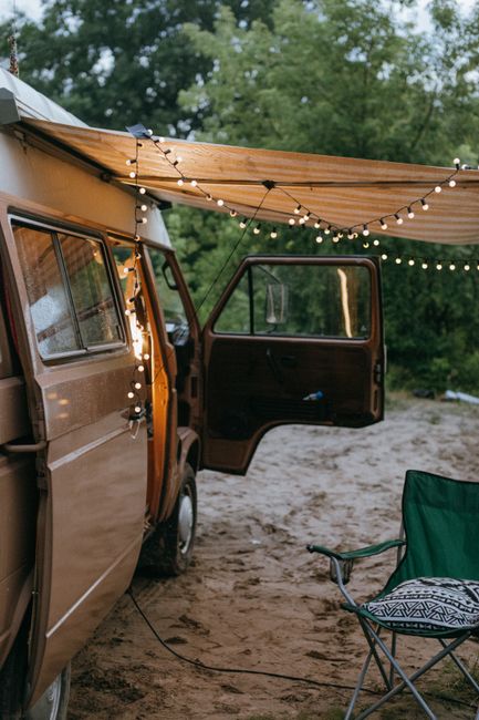 A cozy car glamping setup at a quiet campsite with string lights and a camp chair beside the vehicle