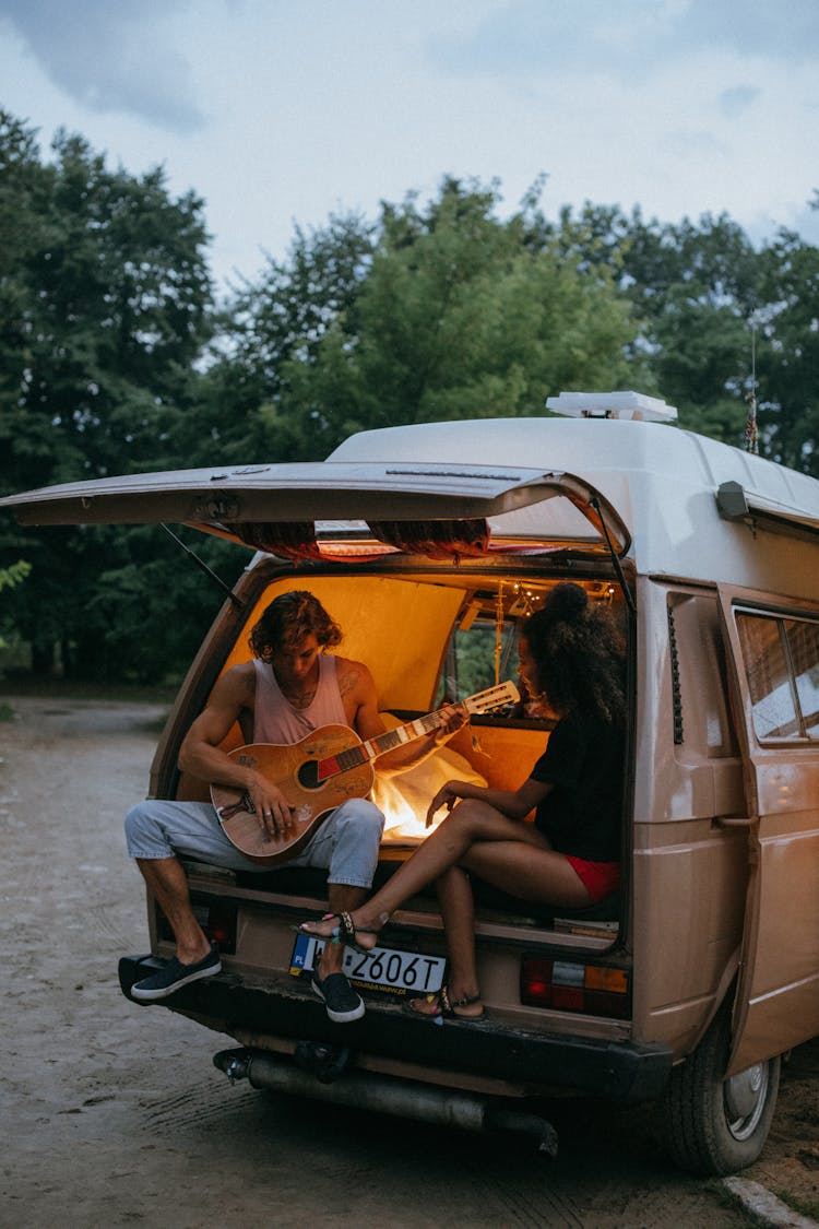 A Man Playing A Guitar And A Woman Sitting In A Van