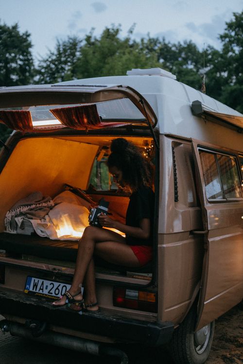 Free Young woman enjoys a quiet evening in a cozy camper van surrounded by nature. Stock Photo