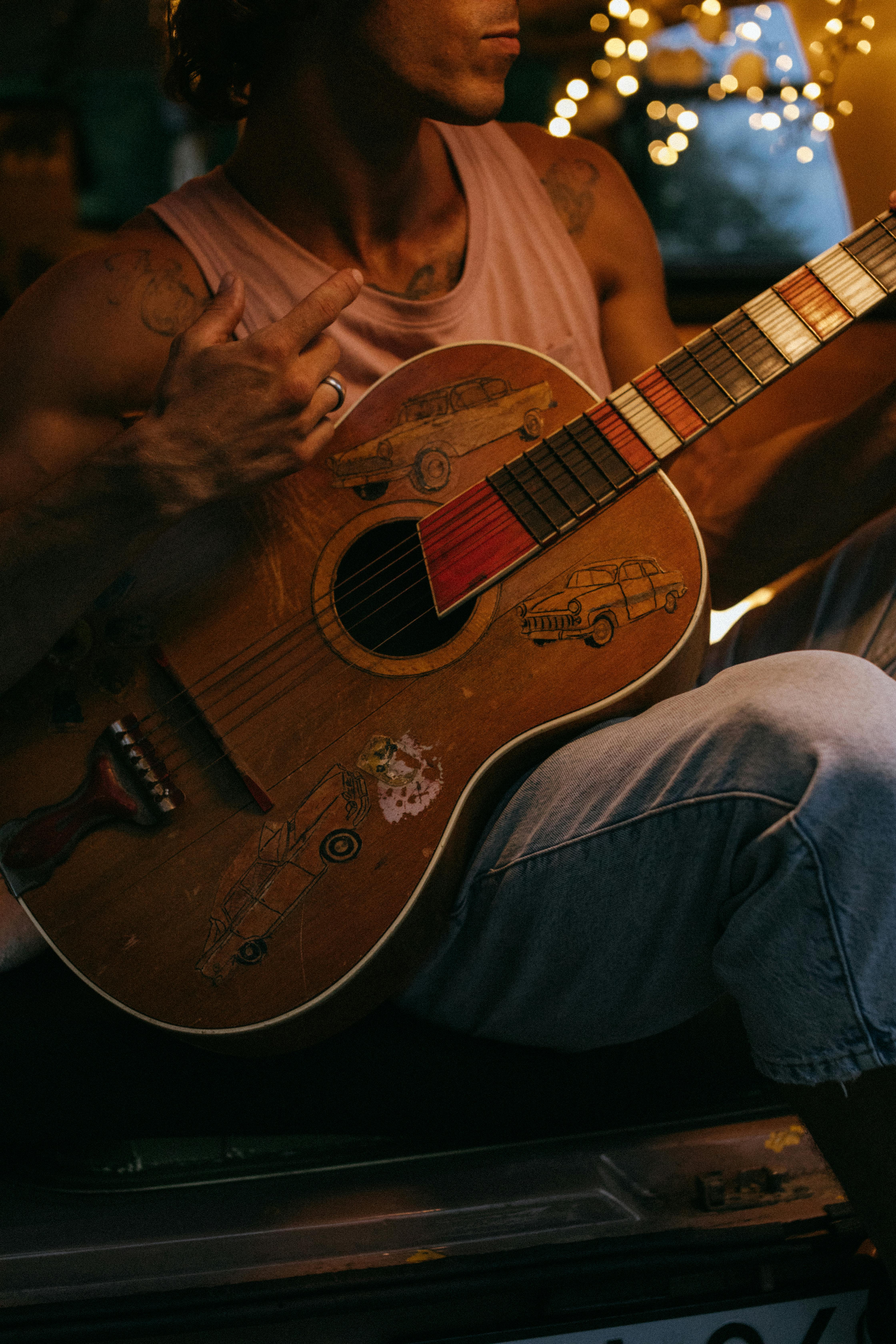 A tattooed guitarist in casual clothing plays an acoustic guitar.