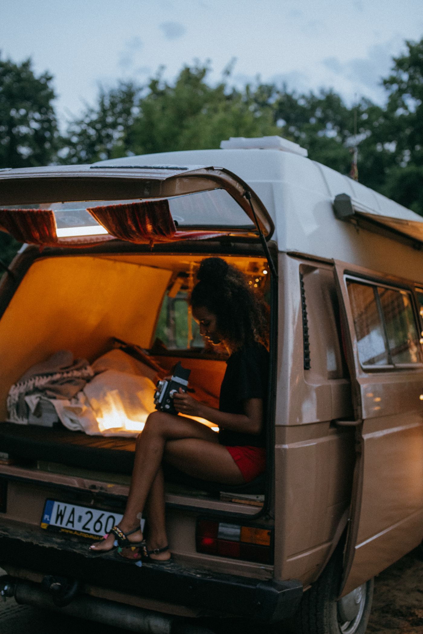 Creator in a campervan at twilight with the interior lit up — shoot and upload from anywhere