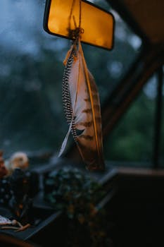 Close-up of feathers hanging from a rearview mirror inside a car during a road trip.