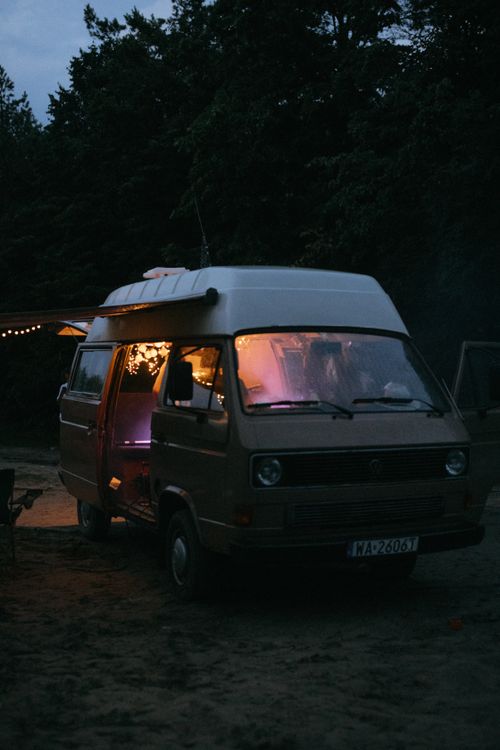 Free A cozy camper van with warm interior lighting parked in a serene forest at twilight. Stock Photo