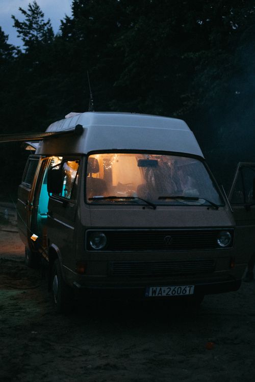 Free A camper van parked at dusk, emitting warm light, creating a cozy atmosphere outdoors. Stock Photo
