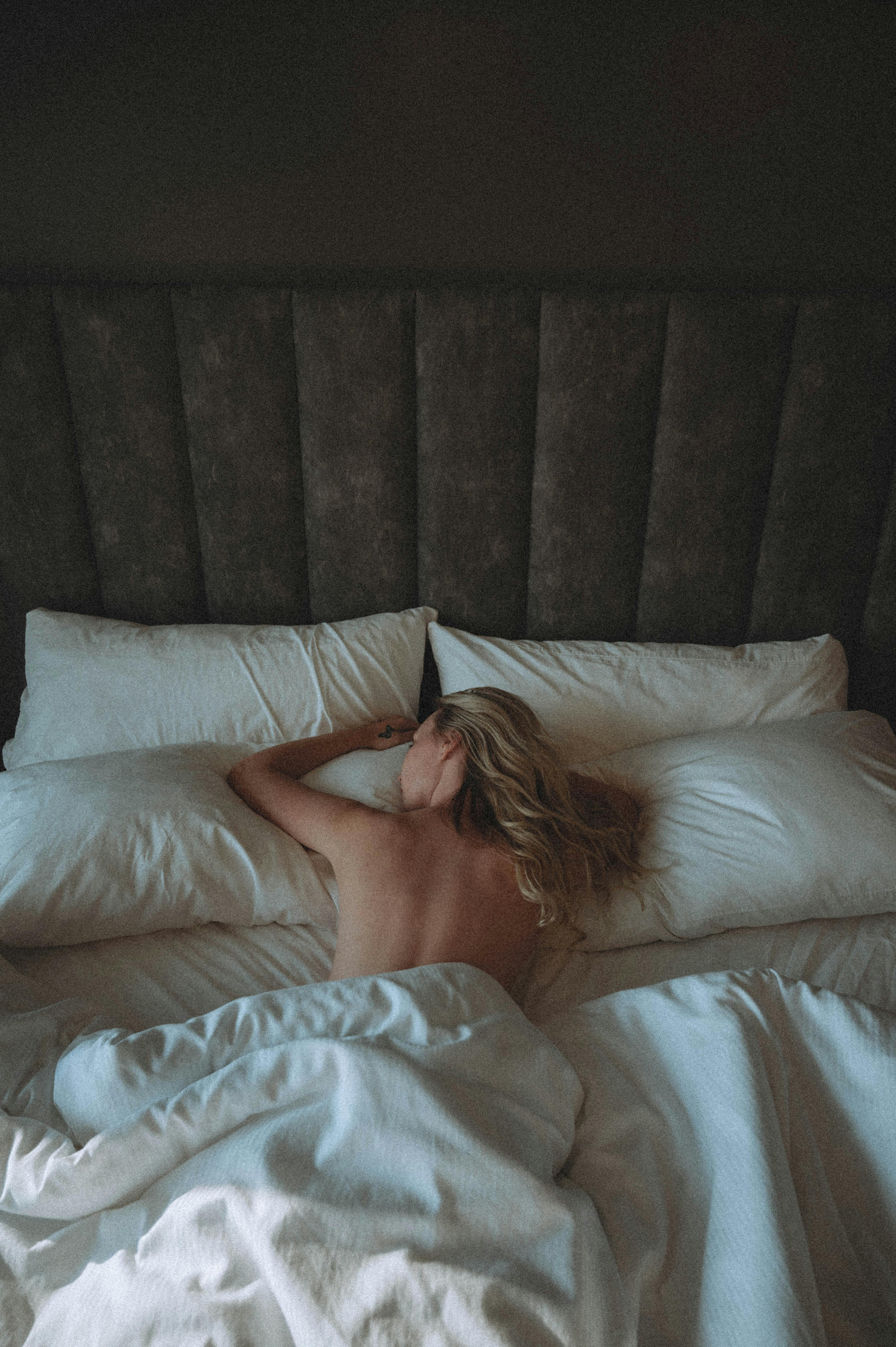 Blonde woman lying topless on a bed, embracing morning tranquility in a cozy bedroom.