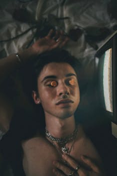 A young adult with pills on closed eyes, lying near a vintage TV, creating a surreal atmosphere.