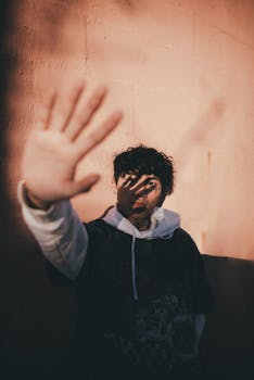 A young man holds up his hand creating a shadow effect on his face against a sunlit wall.