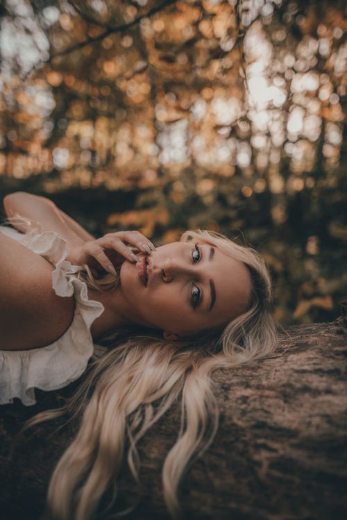 Free A calm and serene portrait of a blonde woman lying on a tree trunk in a forest setting, capturing a peaceful moment. Stock Photo