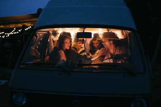 Friends enjoying a cozy night inside a decorated camper van, surrounded by outdoor adventure vibes.