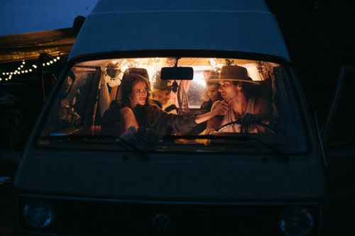 Free A cozy evening scene with a couple sharing a moment in a vintage van lit by string lights. Stock Photo