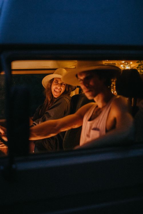 Free Young couple enjoying a playful road trip at night inside their van. Stock Photo