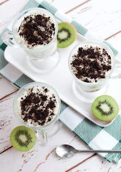 Creamy desserts topped with chocolate crumbs and kiwis on a white tray.