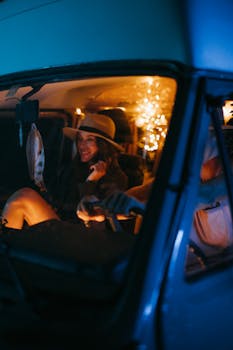 A couple enjoys a cozy night drive in a vintage van adorned with warm fairy lights.