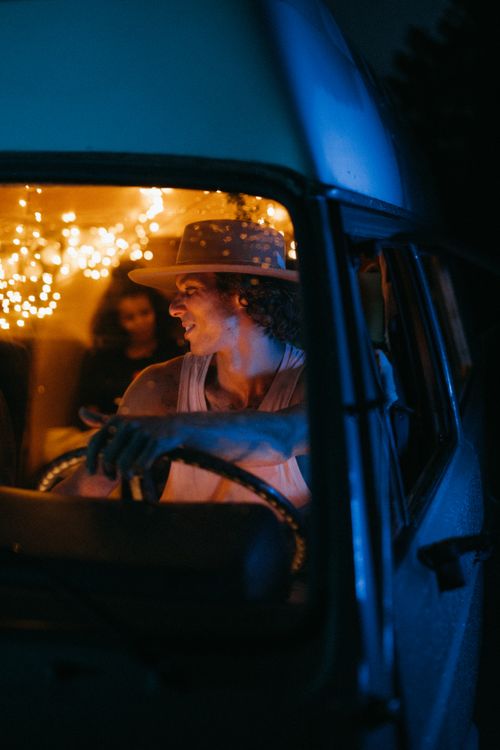 Free Man in a hat driving a van at night with festive interior lights, smiling. Stock Photo