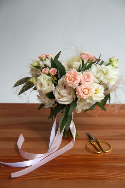 Charming bridal bouquet with white and pink roses on a wooden surface with scissors.