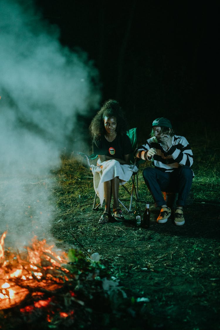 Man And Woman Sitting Near A Campfire During The Night