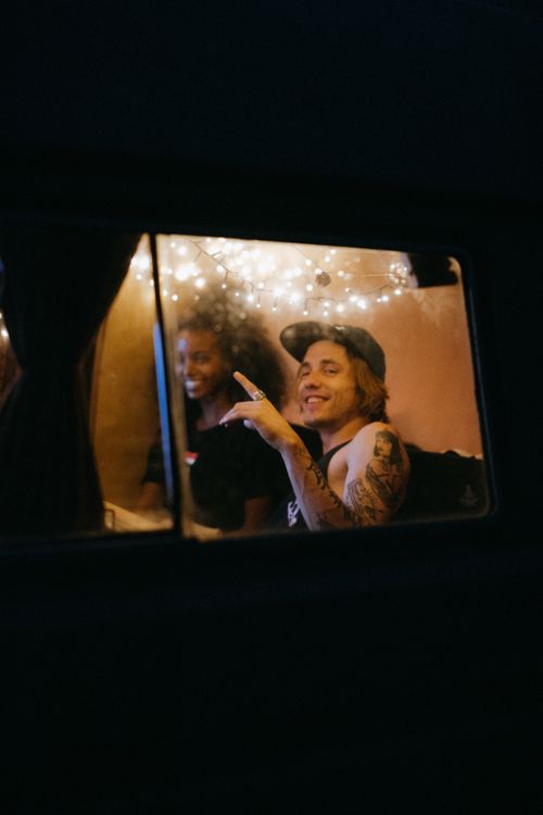 Free Two young adults relax inside a decorated camper van, enjoying a cozy and adventurous night. Stock Photo