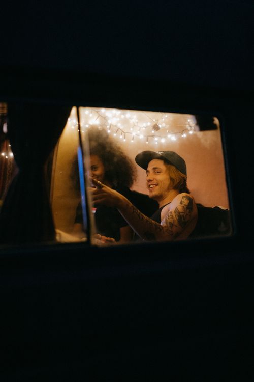 Free Friends relaxing in a van with warm lights, tattoos visible, creating a cozy, adventurous atmosphere. Stock Photo