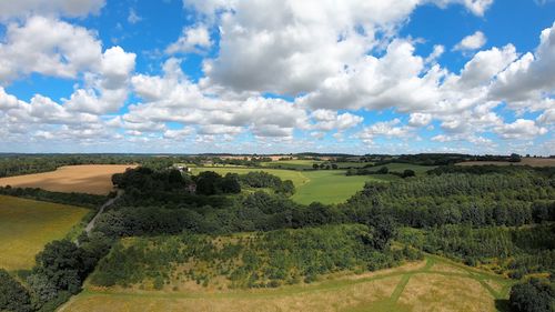 Free Lush green fields and forests under a bright blue sky with clouds, captured from above in the UK. Stock Photo