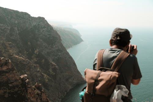 Man Standing on a Cliff Looking at View of Mountain and Seascape