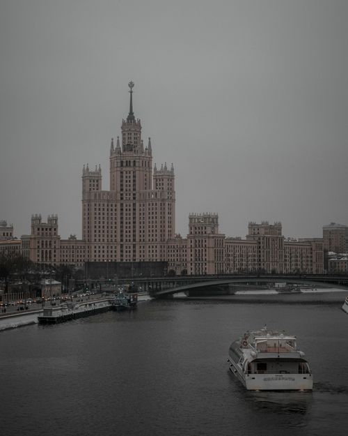 Free Stunning view of Moscow's neo-Gothic skyscraper along the Moskva River, featuring a serene ferry passing by. Stock Photo