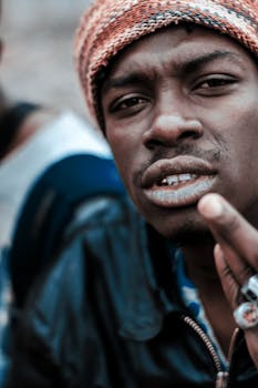 Close-up portrait of a young black man wearing a knit hat and leather jacket, expressing attitude.