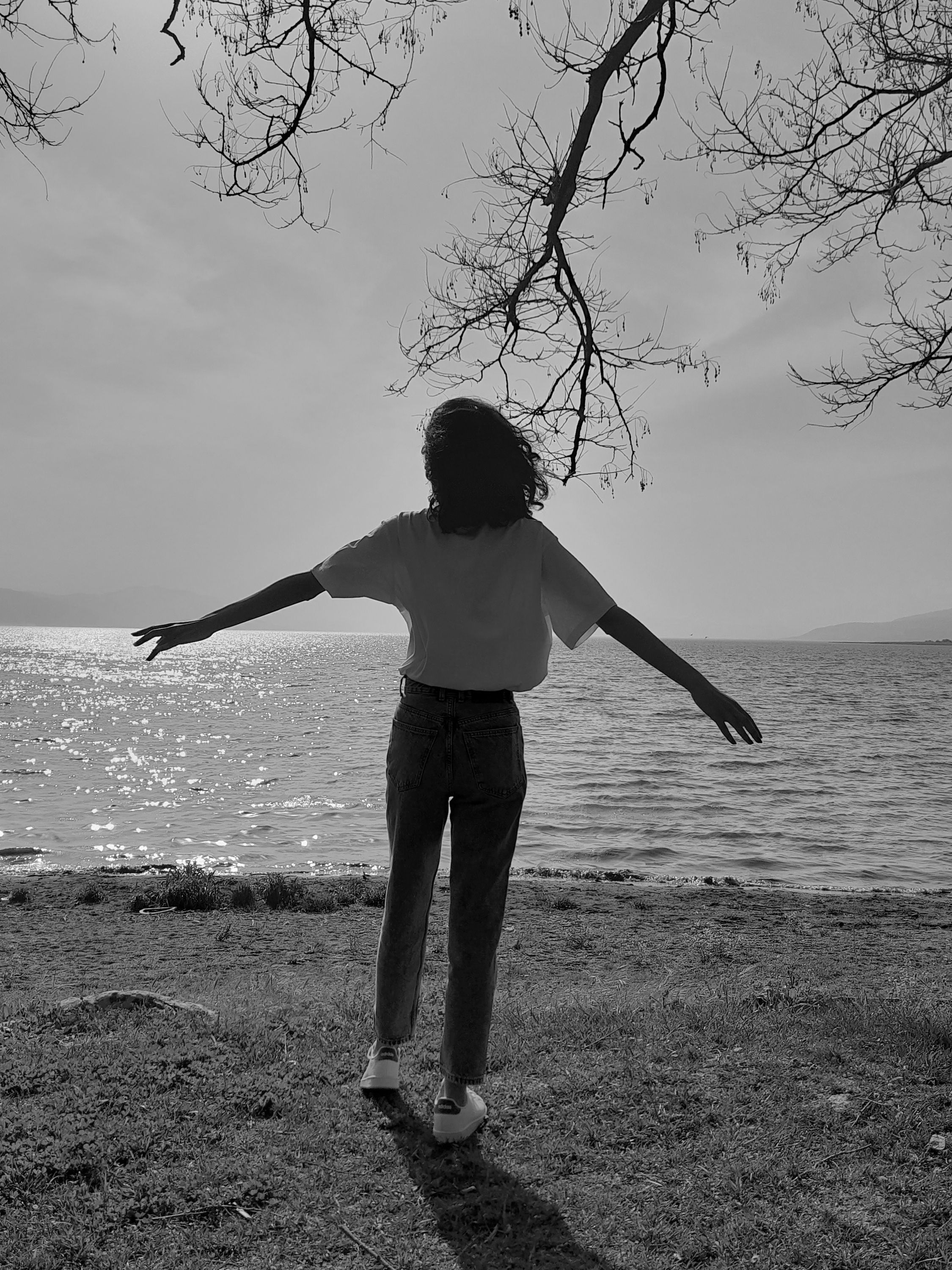 A silhouette of a woman with open arms by the sea, embracing nature.