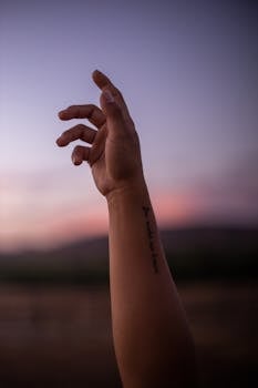 Close-up of a tattooed hand reaching out against a vibrant sunset in San Diego, CA.