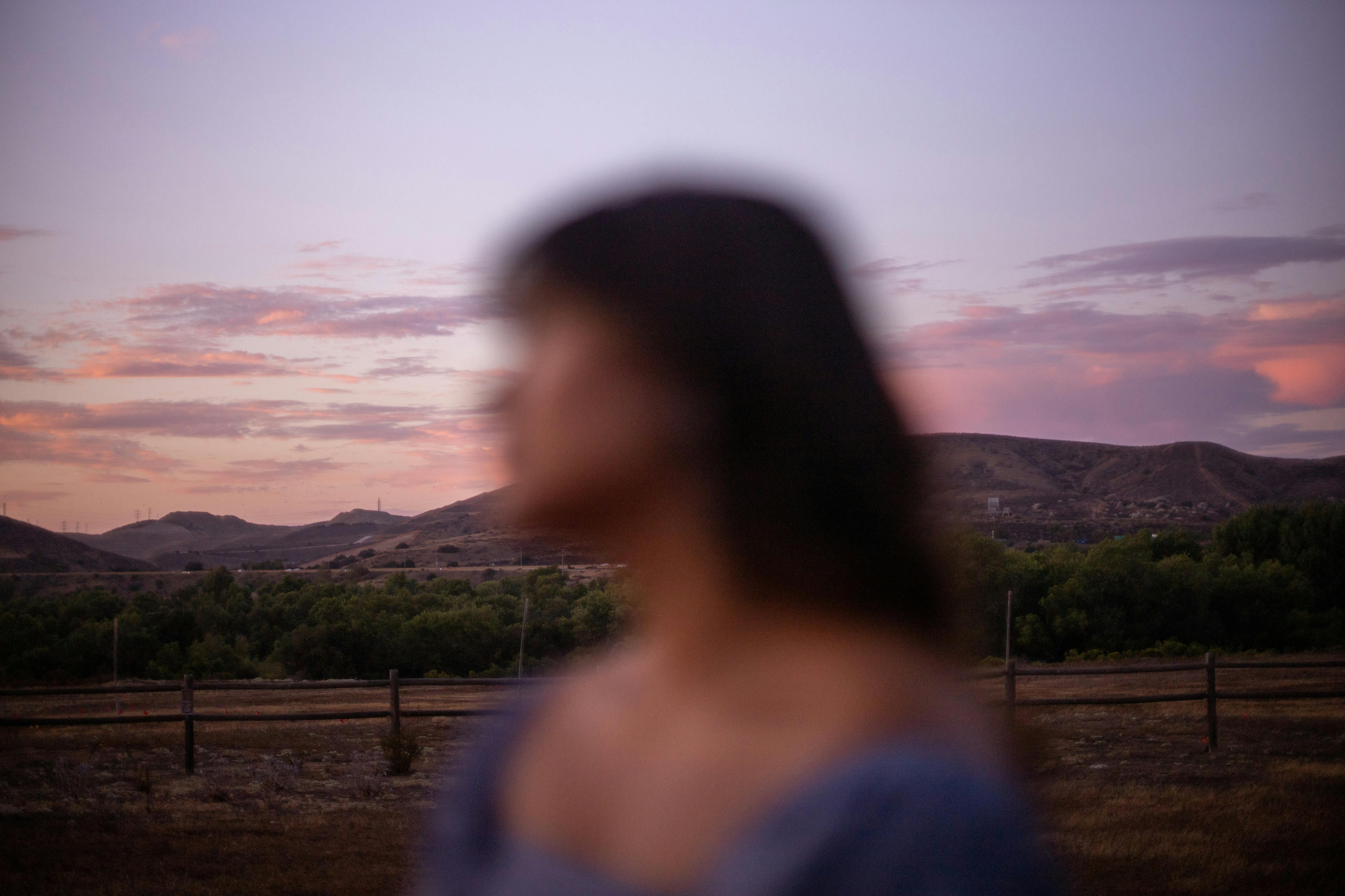 A blurred portrait of a woman against a scenic San Diego sunset with hills and vibrant sky.