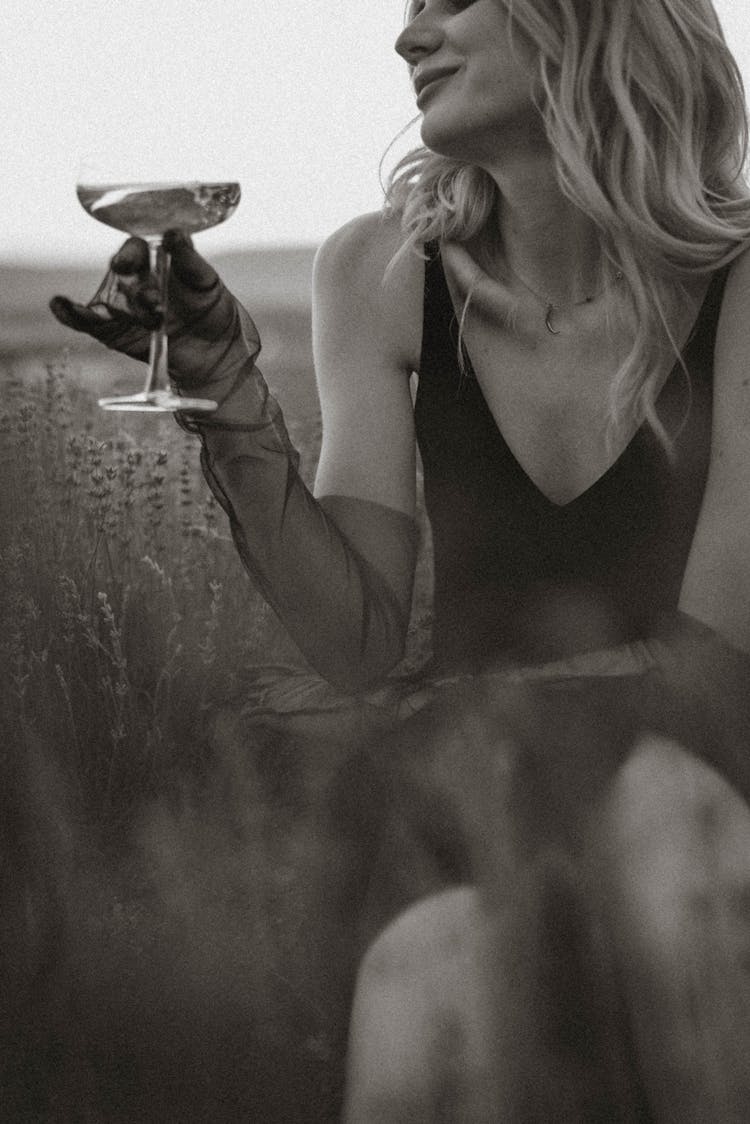 Woman In Black Tank Dress And Gloves Holding Wine Glass While Sitting In Grass