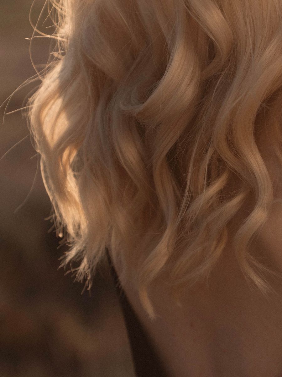 Cabelo loiro cacheado com mechas iluminadas pela luz dourada