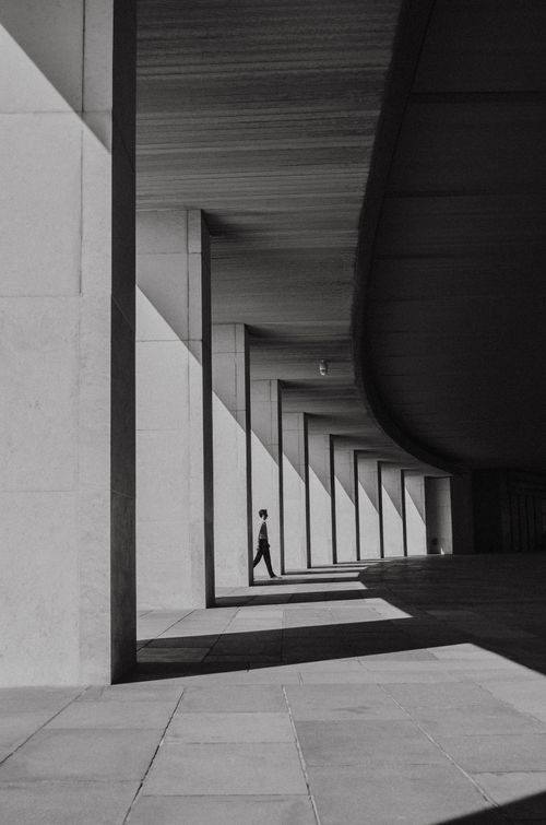 Free Black and white photo of a person walking through a modern architectural corridor. Stock Photo