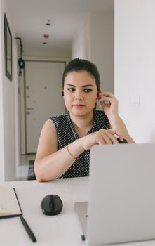 Focused woman adjusting wireless earphones while working on a laptop from home.