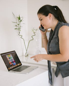 Woman in polka dots working from home with laptop and phone in a modern setup.