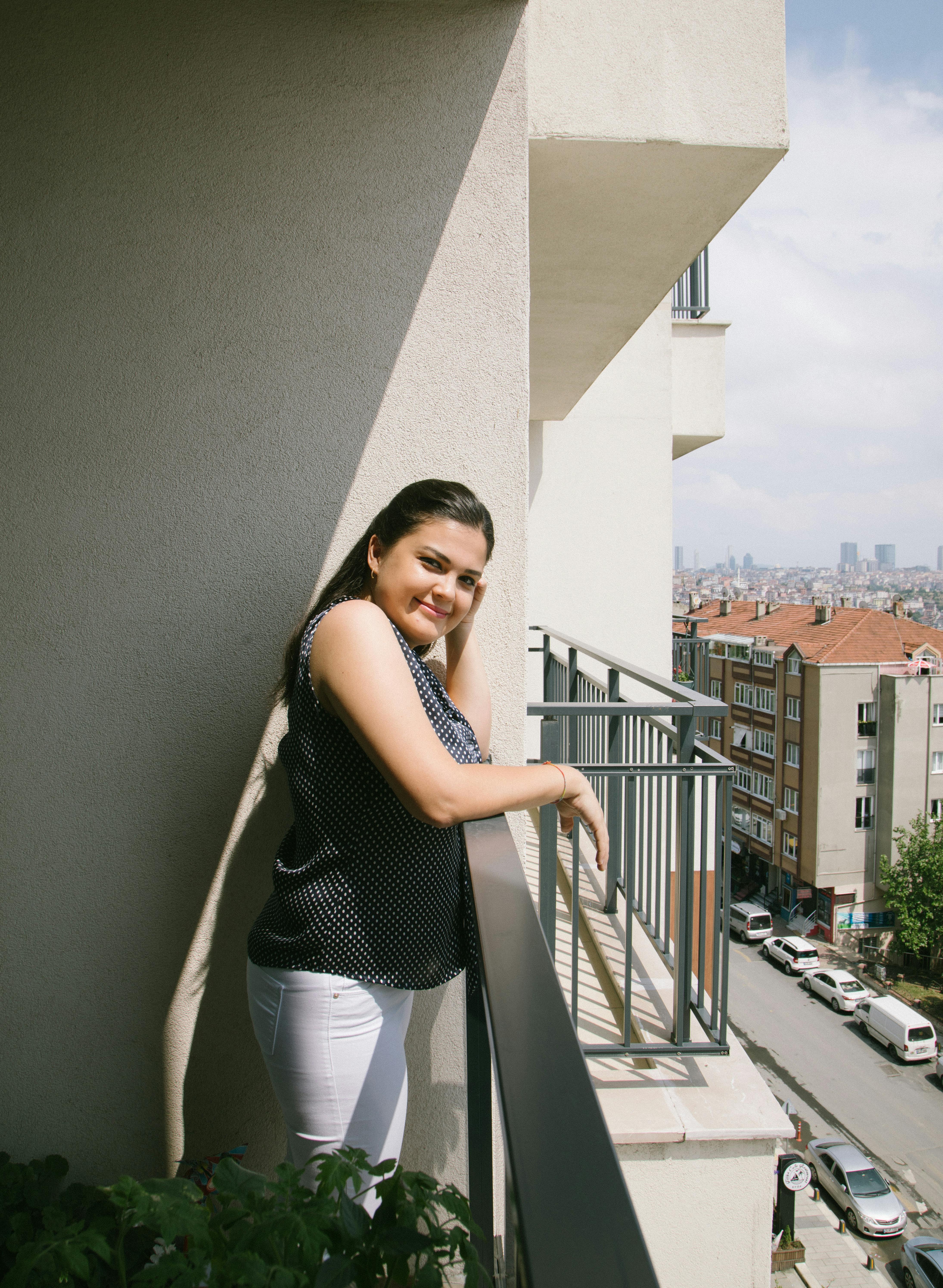 A woman smiles on a balcony in İstanbul, overlooking the cityscape on a sunny day.