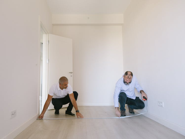 Two Men Measuring Length Of The Empty Room With White Walls