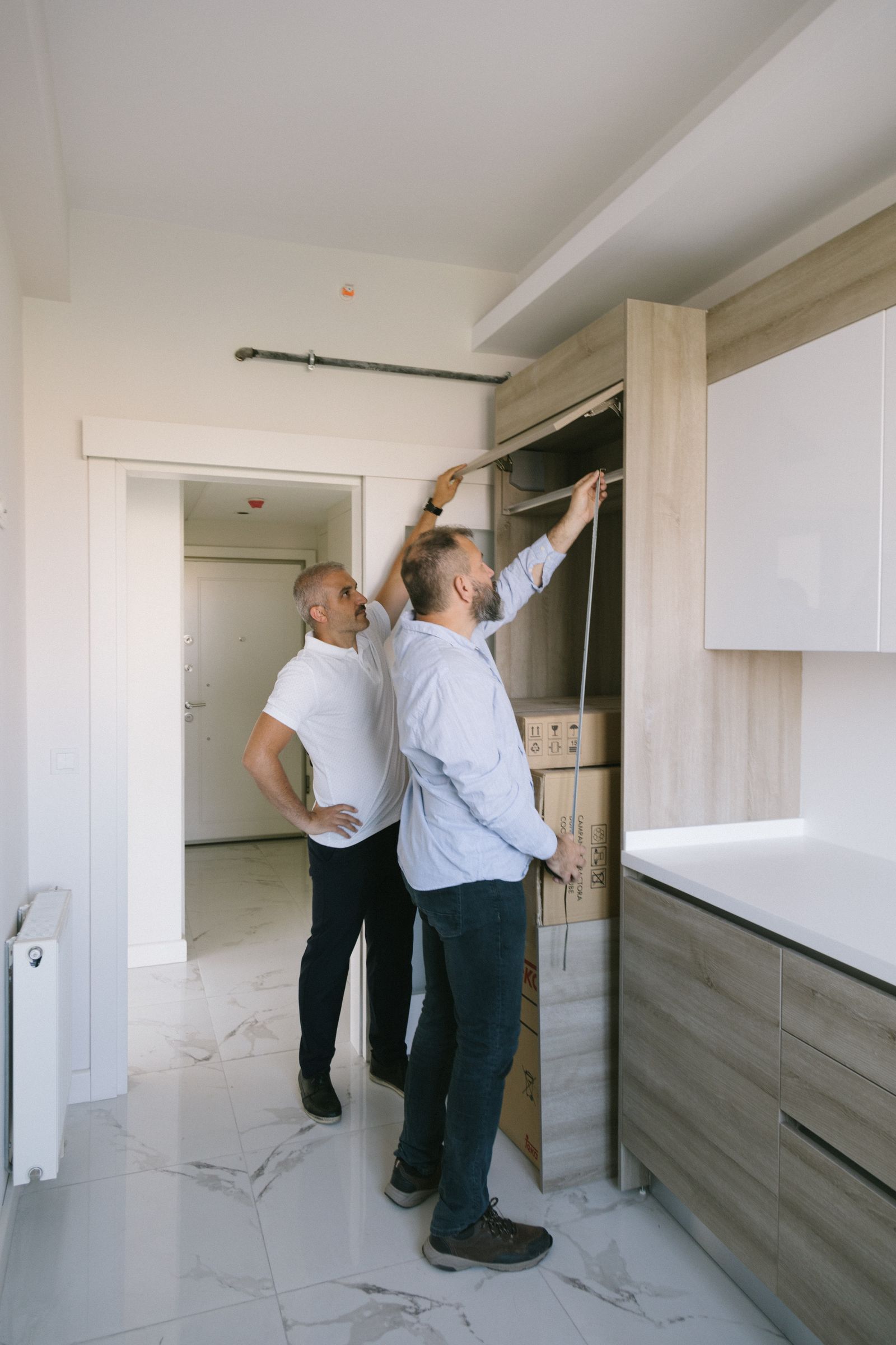 Two people measuring a kitchen cabinet during an installation review