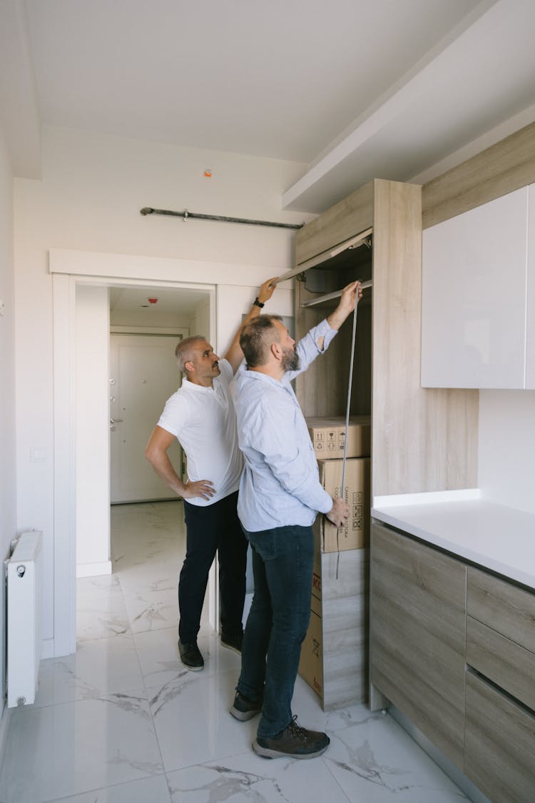 Man Measuring A Cabinet With Another Man