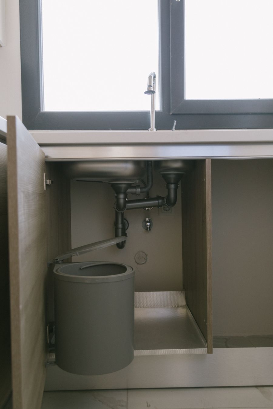 open under-sink cabinet showing plumbing space for organizer clearance
