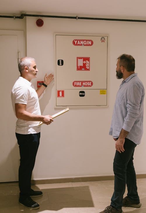 Free Two Men Standing Near a Fire Hose Metal Cabinet Stock Photo