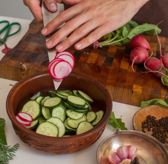 A close-up of slicing fresh cucumbers and radishes for a salad in a kitchen setting.